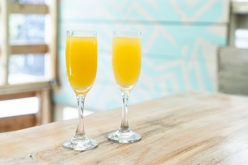 Two glasses of mimosas on top of a wooden table